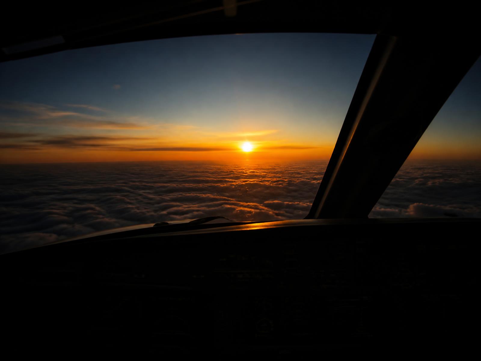 View from an airliner cockpit at sunset above the clouds